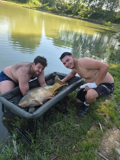 Due pescatori con una carpa sulla culla di slamatura vicino all'acqua