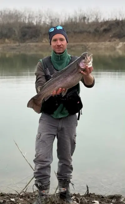 Pescatore con una grossa trota iridea in riva al lago
